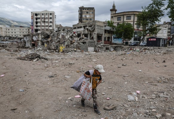 epa10611950 A Syrian child collects plastic next to damaged buildings in Kahramanmaras, Turkey, 06 May 2023. More than 50,000 people died and thousands more were injured after major earthquakes struck ...