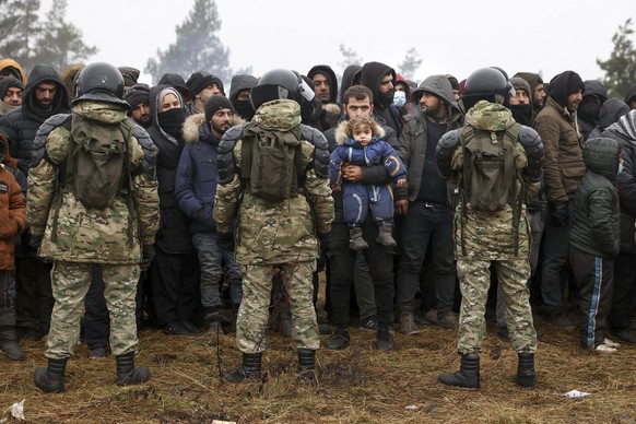 Migrants from the Middle East and elsewhere in front of Belarusian servicemen as they gather at the Belarus-Poland border near Grodno, Belarus, Sunday, Nov. 14, 2021.Poland&#039;s prime minister says  ...