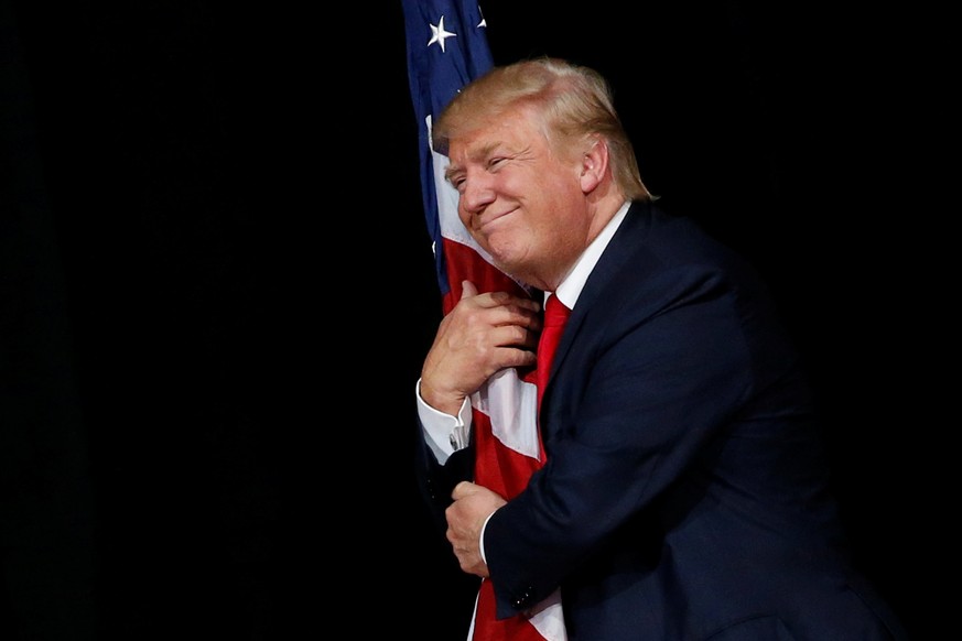 Republican U.S. presidential nominee Donald Trump hugs a U.S. flag as he comes onstage to rally with supporters in Tampa, Florida, U.S. October 24, 2016. REUTERS/Jonathan Ernst