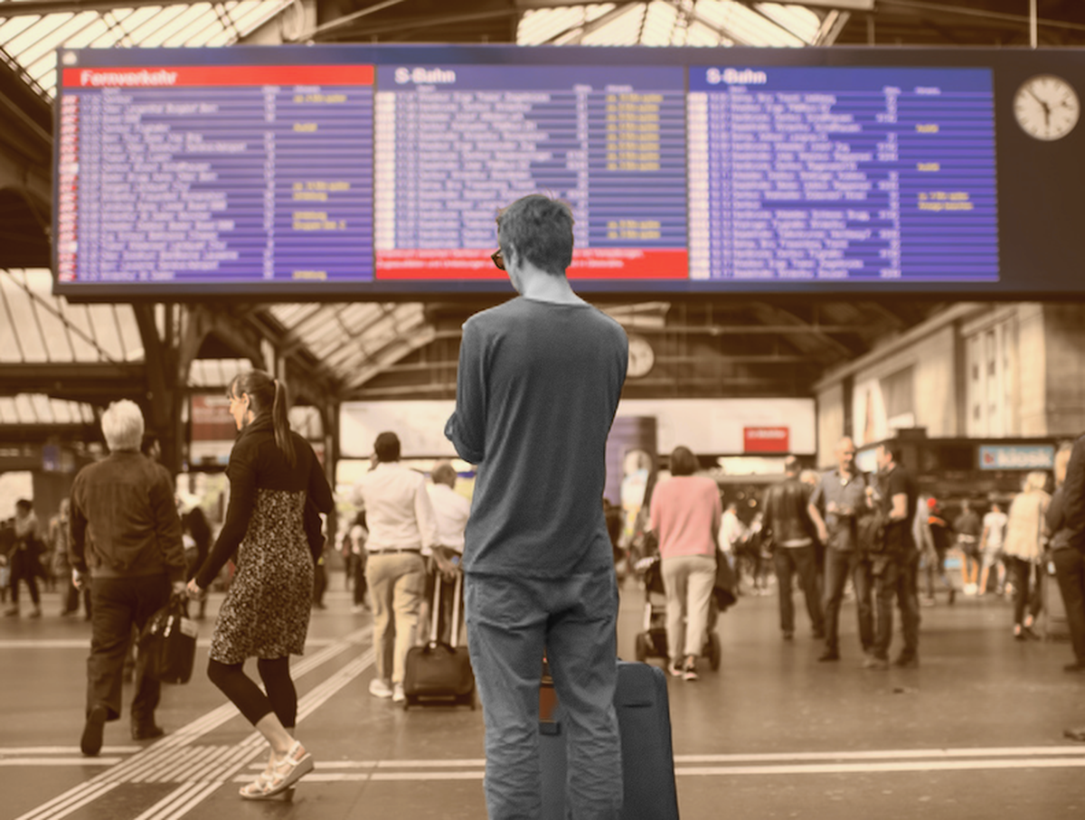 Un individu devant le grand panneau CFF de la gare de Zurich.