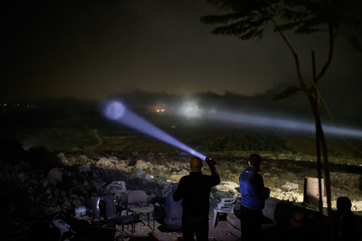 A Palestinian scans a valley with a flashlight as cars move on the top of a hill during a volunteer night watch to help prevent Israeli settler attacks in the West Bank town of Sinjil, Wednesday, Sept ...