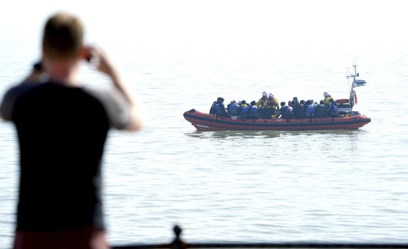 A man watches a group of people thought to be migrants as they are brought to shore in Kingsdown, after being intercepted by an RNLI crew following a small boat incident in the Channel, in Kent, Engla ...