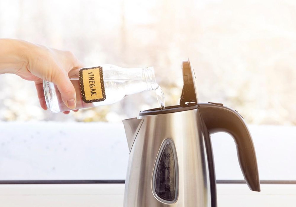 Woman pouring natural destilled acid white vinegar in electric kettle to remove boil away the limescale. Descaling a kettle, remove scale concept.

mit essig den wasserkocher reinigen