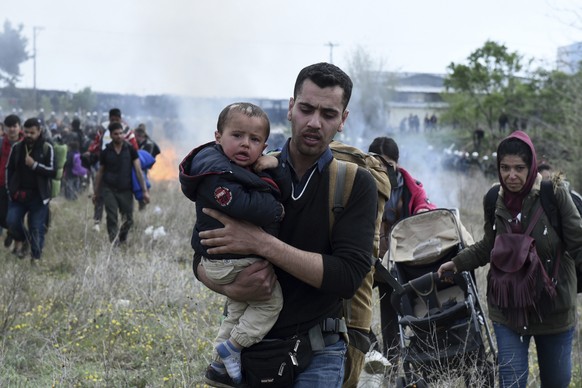 A man holds a baby as riot police use tear gas during clashes outside a refugee camp in the village of Diavata, west of Thessaloniki, northern Greece, Friday, April 5, 2019. Clashes broke out Thursday ...