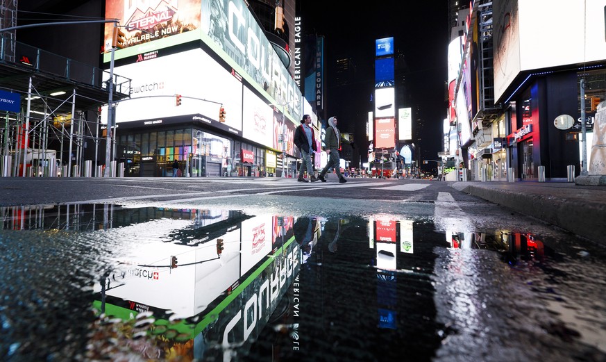 epa08323075 People walk through a nearly empty Times Square in New York, USA, 25 March 2020. A statewide shut down of all non-essential businesses and a ban on all non-solitary outside activities is c ...