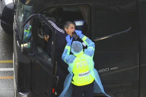 A man conducts a COVID-19 test on a driver at the Port of Dover in Kent, England, Thursday Dec. 24, 2020 where thousands wait to resume their journey across The Channel after the borders with France reopened. Trucks inched slowly past checkpoints in Dover and headed across the Channel to Calais on Thursday after France partially reopened its borders following a scare over a rapidly spreading new virus variant.(Aaron Chown/PA via AP)