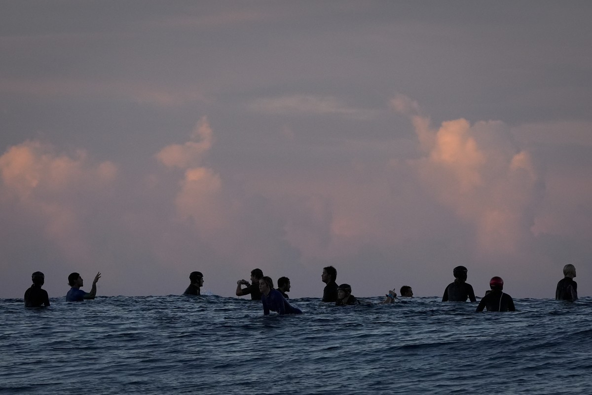Surfers talk in the lineup before the start of the third round of surfing competition at the 2024 Summer Olympics, Monday, July 29, 2024, in Teahupo'o, Tahiti. (AP Photo/Gregory Bull)