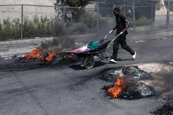 epa11217538 A person pushes a cart past tires set on fire by demonstrators during a protest in Port-au-Prince, Haiti, 12 March 2024. According to a statement by the Caribbean Community and Common Mark ...