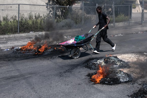 epa11217538 A person pushes a cart past tires set on fire by demonstrators during a protest in Port-au-Prince, Haiti, March 12, 2024. According to a statement from the Caribbean Community and Common Mark…