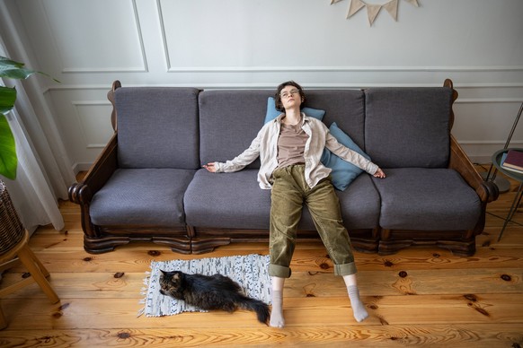 Depression Einsamkeit, emotionaler Niedergang und Isolation zu Hause mit Katze. Frau streckt Arme auf Sofa aus Depression Einsamkeit, emotionaler Niedergang und Isolation zu Hause mit Katze. Frau stre ...