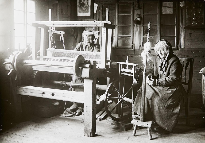 Zwei Frauen in der Stube an der Arbeit: die eine am Spinnrad, die andere am Webstuhl, um 1890.