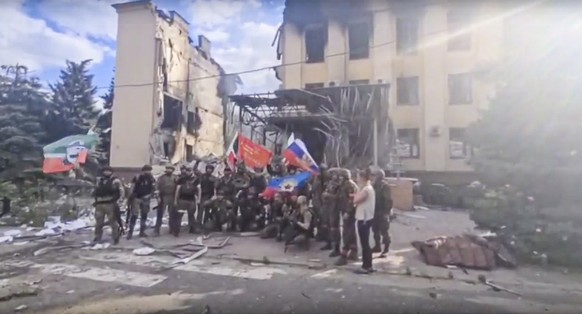 This photo taken from video provided by Ramzan Kadyrov's Official Telegram channel released on Saturday, July 2, 2022 shows Russian troops including soldiers of Chechen regiment waving Russian and Chechen republic national flags as they pose for a photo in front of a destroyed building in Lysychansk, Ukraine. (Ramzan Kadyrov's Official Telegram channel via AP)