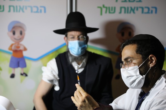 epa08937702 An ultra-orthodox Jewish man receives a coronavirus COVID-19 pandemic vaccine by a male nurse in Jerusalem, Israel, 14 January 2021. Media report that Israel is on a massive nationwide COV ...