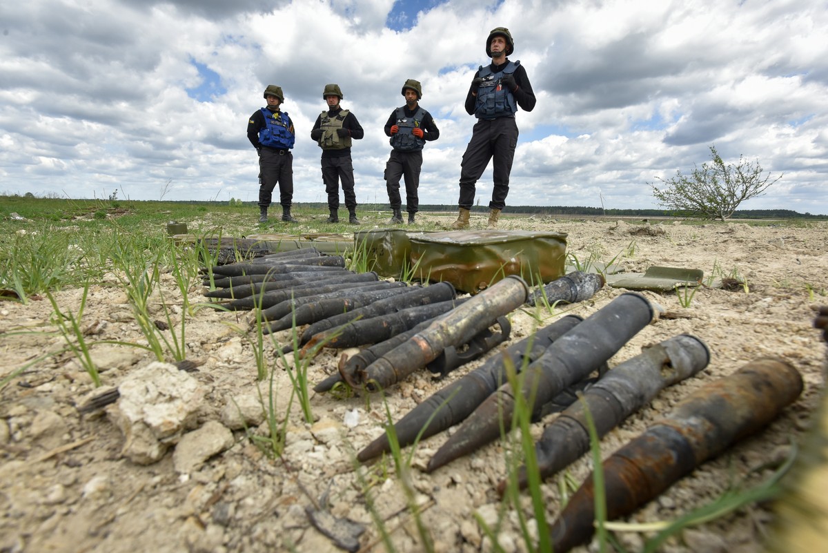 epa09980139 Members of the Special Demining Unit of the State Emergency Service of Ukraine stand near explosive devices arranged in line on the ground during demining works on the outskirts of Borodya ...