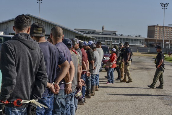 Workers stand handcuffed after being arrested by U.S. Immigration and Customs Enforcement, ICE, at Delta Downs Racetrack, Hotel and Casino in Calcasieu Parish, near Vinton, La., on Wednesday, June 18, ...