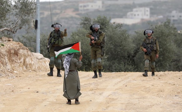 epa10567363 An Israeli soldier (C) points his gun at a Palestinian man holding the Palestinian flag during clashes following a protest against Israeli settlers near the Avitar illegal outpost near Beit...