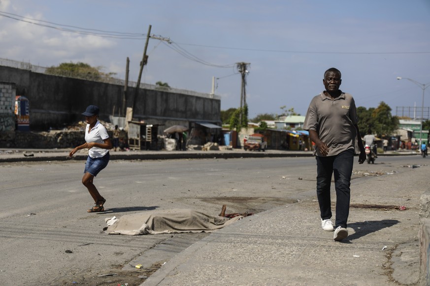 People walk past a body covered by a cloth in Port-au-Prince, Haiti, Wednesday, March 6, 2024. (AP Photo/Odelyn Joseph)