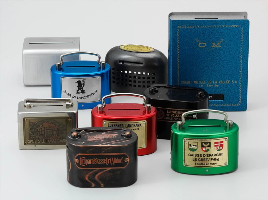Verschiedene Sparkässeli des 20. Jahrhunderts, hinten rechts ein Exemplar für das Büchergestell.