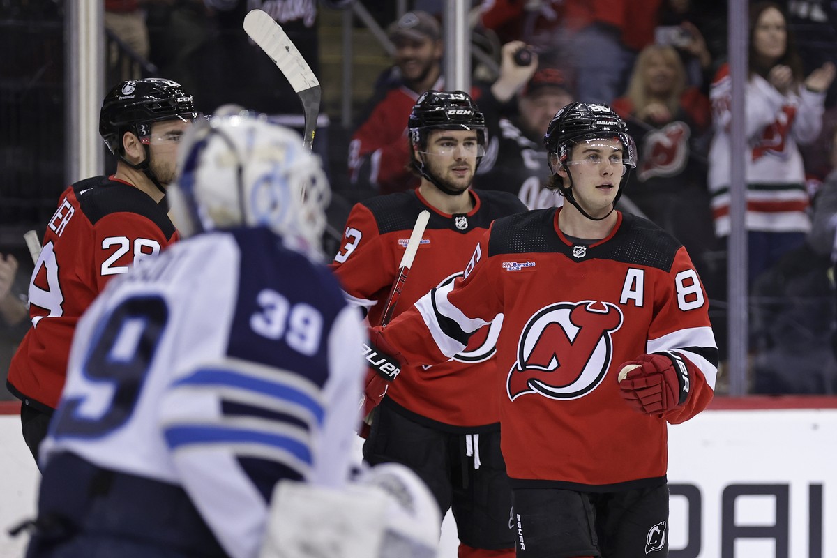New Jersey Devils center Jack Hughes, right, reacts after scoring a goal past Winnipeg Jets goaltender Laurent Brossoit during the second period of an NHL hockey game Thursday, March 21, 2024, in Newa ...