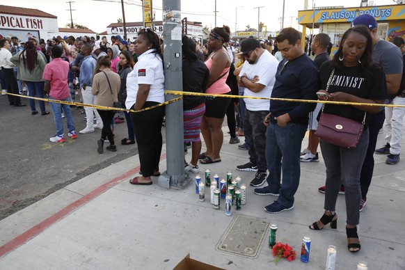People set candles behind police yellow tape next to the Marathon Clothing store of rapper Nipsey Hussle in Los Angeles, Sunday, March 31, 2019. (AP Photo/Damian Dovarganes)