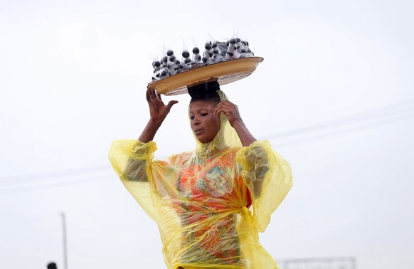 epa08657454 A woman wearing a reflective rain jacket carries walnuts arranged in a tray along a road during rainfall in Lagos, Nigeria, 09 September 2020. Rainfall prediction for Lagos for the rest of ...