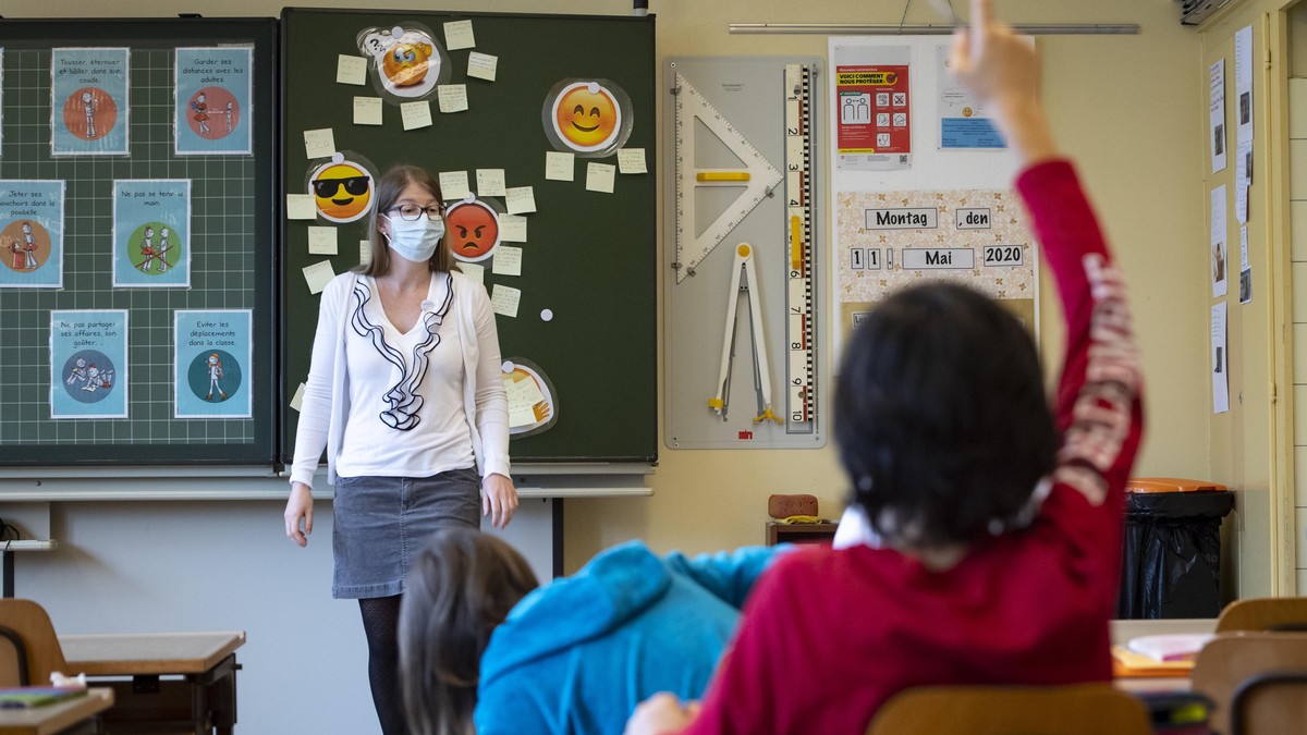 A teacher wearing protective face mask as she teaches close to pupils at a primary school in Morges, Switzerland, Monday, May 11, 2020. Swiss primary and secondary schools reopened with half of the st ...