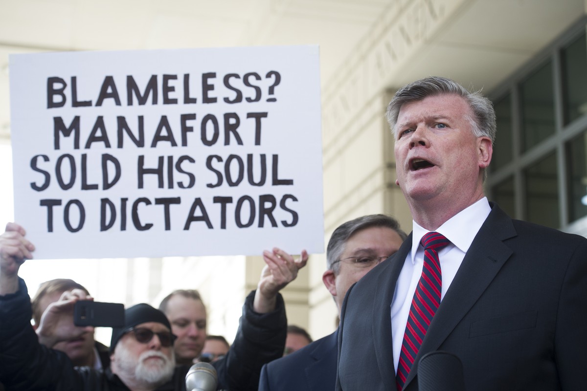 A protester holds a sign as Kevin Downing, Paul Manafort's defense attorney, speaks to reporters after Manafort was sentenced at the U.S. District Court in Washington, Wednesday, March 13, 2019.  ...