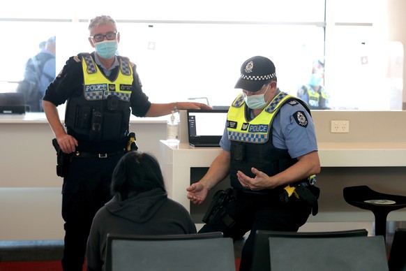 epa09416043 WA Police are seen talking to a passenger who arrived from Sydney at Perth Airport, Perth, Australia, 16 August 2021. Western Australia will require arrivals from NSW to provide evidence t ...