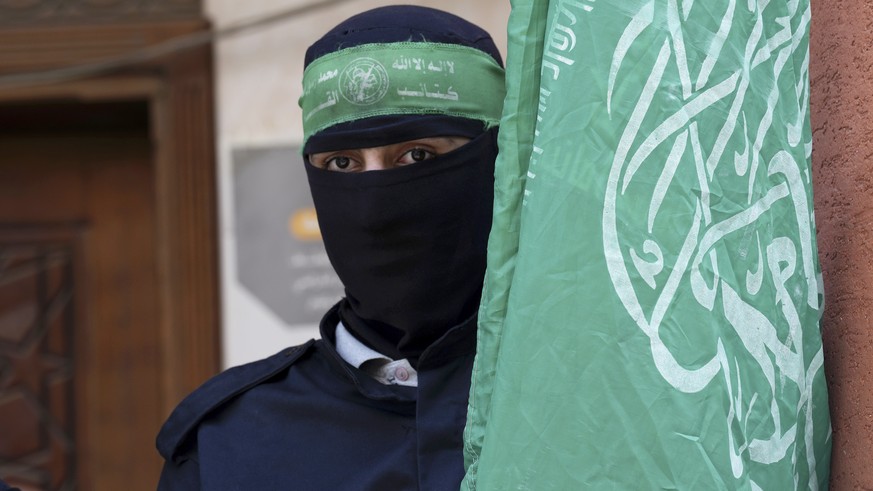 Masked militant from the Izzedine al-Qassam Brigades, the military wing of Hamas, waves the green flag of the Islamist group during a protest in support of Palestinian prisoners in Israeli jails, afte ...
