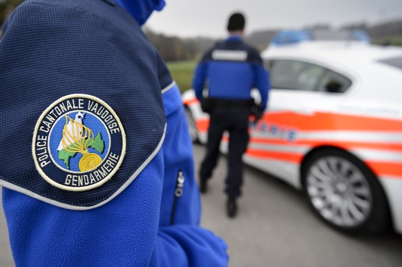 [Editor&#039;s note: photo mise-en-scene] Detail view of the uniform of a police officer of the cantonal police of Vaud, in the foreground, and another cantonal police officer next to a police car, in ...