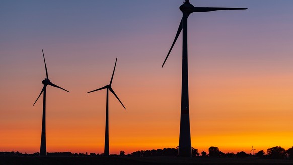Windraeder sind vor einem farbenpraechtig leuchtenden Morgenhimmel kurz vor Sonnenaufgang zu sehen, am Freitag, 26. Juli 2019, in Mallnow, Deutschland. Auch am Freitag soll es vielerorts in Deutschlan ...