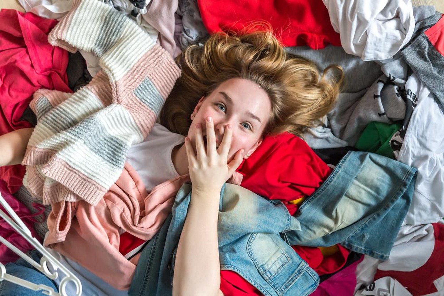 Fast fashion, the girl puts things in order in the closet. A bunch of colorful clothes. The concept of processing, second hand, eco, minimalism, consumption of goods.