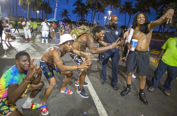 epa09102418 People pose next to a police officer as he enforces the South Beach 8pm curfew during the spring break in Miami Beach, Florida, USA, 27 March 2021. On 20 March the city of Miami Beach impo ...