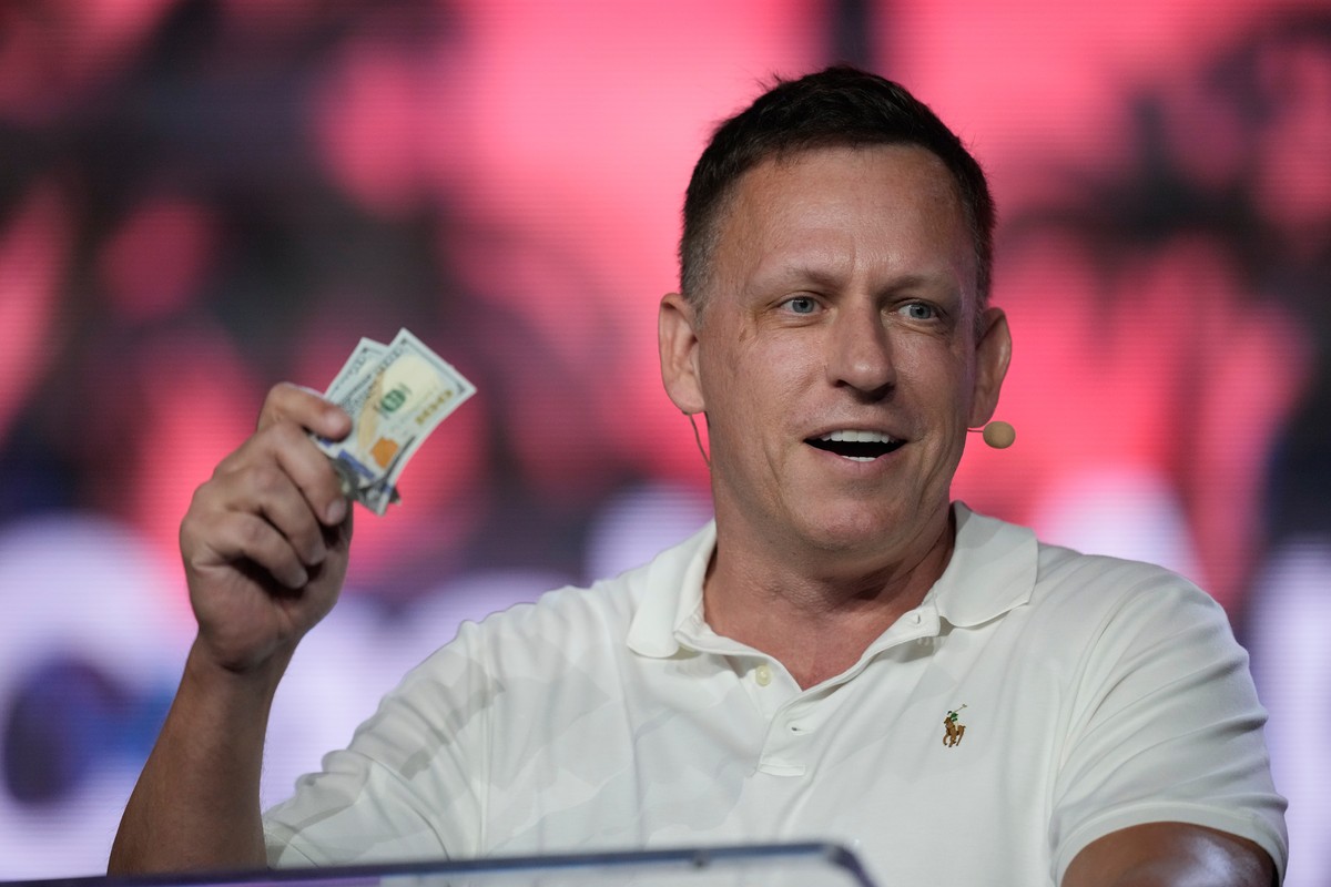 FILE - Peter Thiel, co-founder of PayPal and Palantir, offers a pair of hundred dollar bills to attendees during a keynote address at the Bitcoin Conference, April 7, 2022, in Miami Beach, Fla. (AP Ph ...