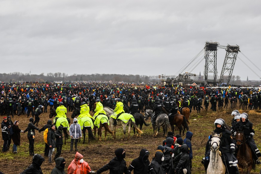 epa10405069 Police officers on horses stand between protesters near the open pit mine with a shovel excavator during a rally of climate protection activists near the village of Luetzerath, Germany, 14 ...