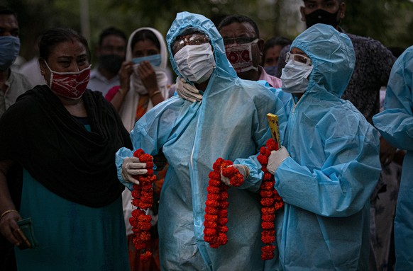 Relatives assist an Indian woman in personal protective equipment offer marigold garlands on the body of her husband .who died of COVID-19 in Gauhati, India, Monday, Sept. 28, 2020. IndiaÄôs confirme ...