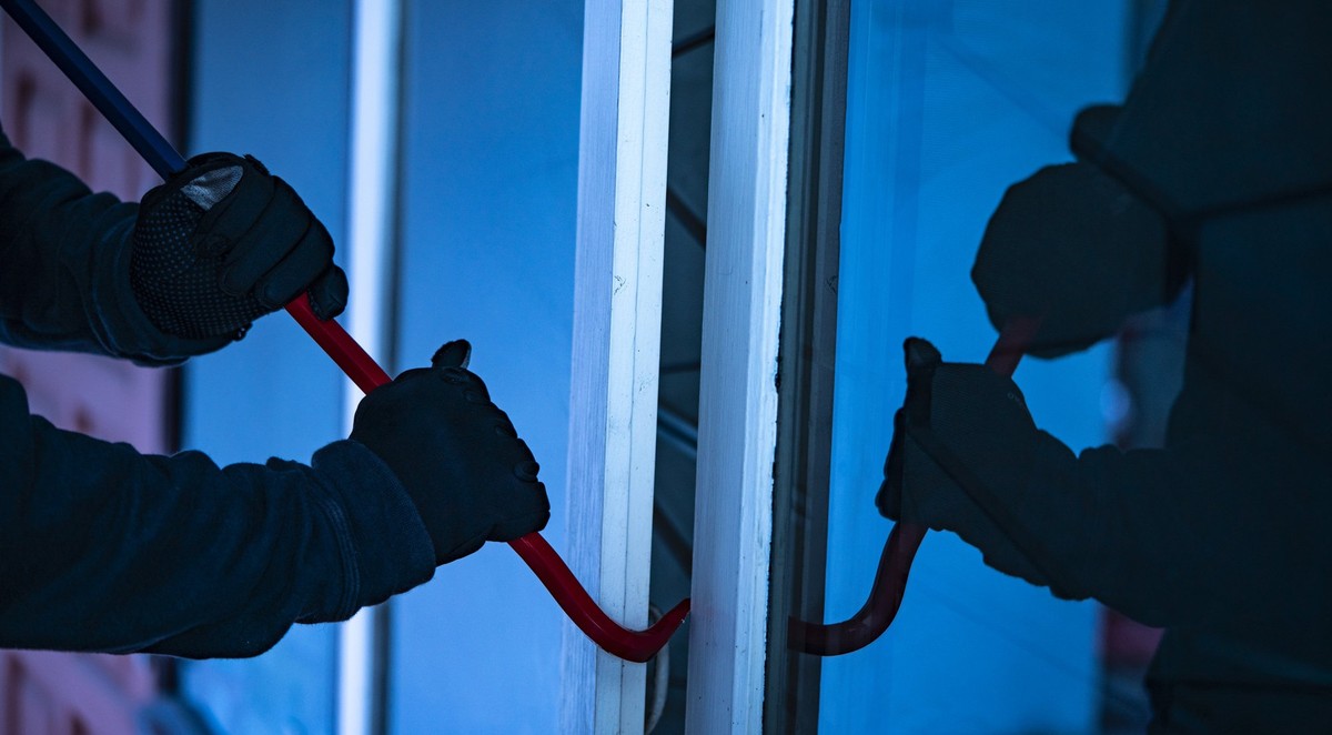 Burglar with crowbar trying break the door to enter the house