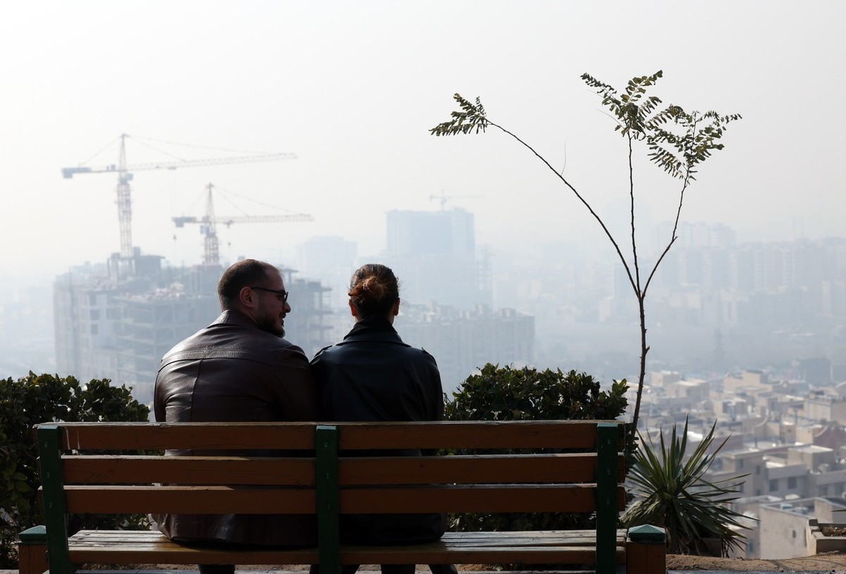 epaselect epa11791666 An Iranian couple sit on a bench in a park as smog obscures the skyline in Tehran, Iran, 24 December 2024. Following heavy air pollution covering in the capital city, the Iranian ...