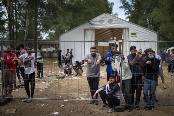 FILE - In this file photo taken on Wednesday, Aug. 4, 2021, Migrants stand by the fence at the at the newly built refugee camp in the Rudninkai military training ground, some 38km (23,6 miles) south f ...