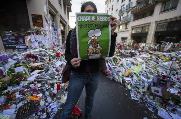 epa04559468 A woman holds the new edition of the French satirical magazine Charlie Hebdo in front of the improvised memorial on Rue Nicolas Appert, near the Charlie Hebdo headquarters, site of the 07  ...