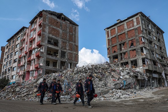 epa10481539 Members of AFAD, the Turkish Disaster and Emergency Management Presidency walk in front of a collapsed building after a powerful earthquake in Hatay, Turkey, 21 February 2023. More than 46 ...