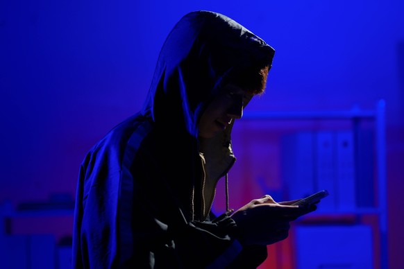 Hacker nutzt Smartphone für Phishing-Angriff und Datendiebstahl in dunkler Cyberumgebung Hacker operating smartphone to execute phishing scheme and steal sensitive information through cyber intrusion  ...