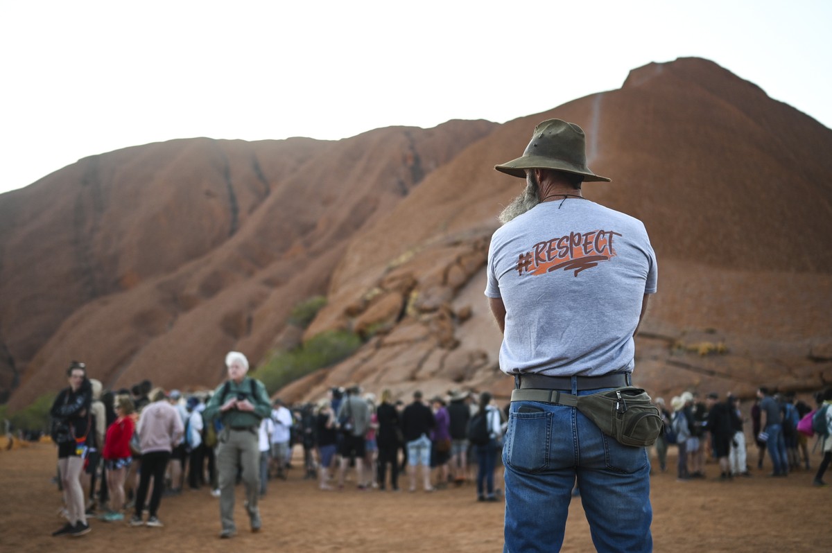 epa07948095 A man looks at tourists lining up to climb Uluru, Australia's iconic sandstone formation, in Uluru-Kata Tjuta National Park in Northern Territory, Australia, 25 October 2019. Tourists ...
