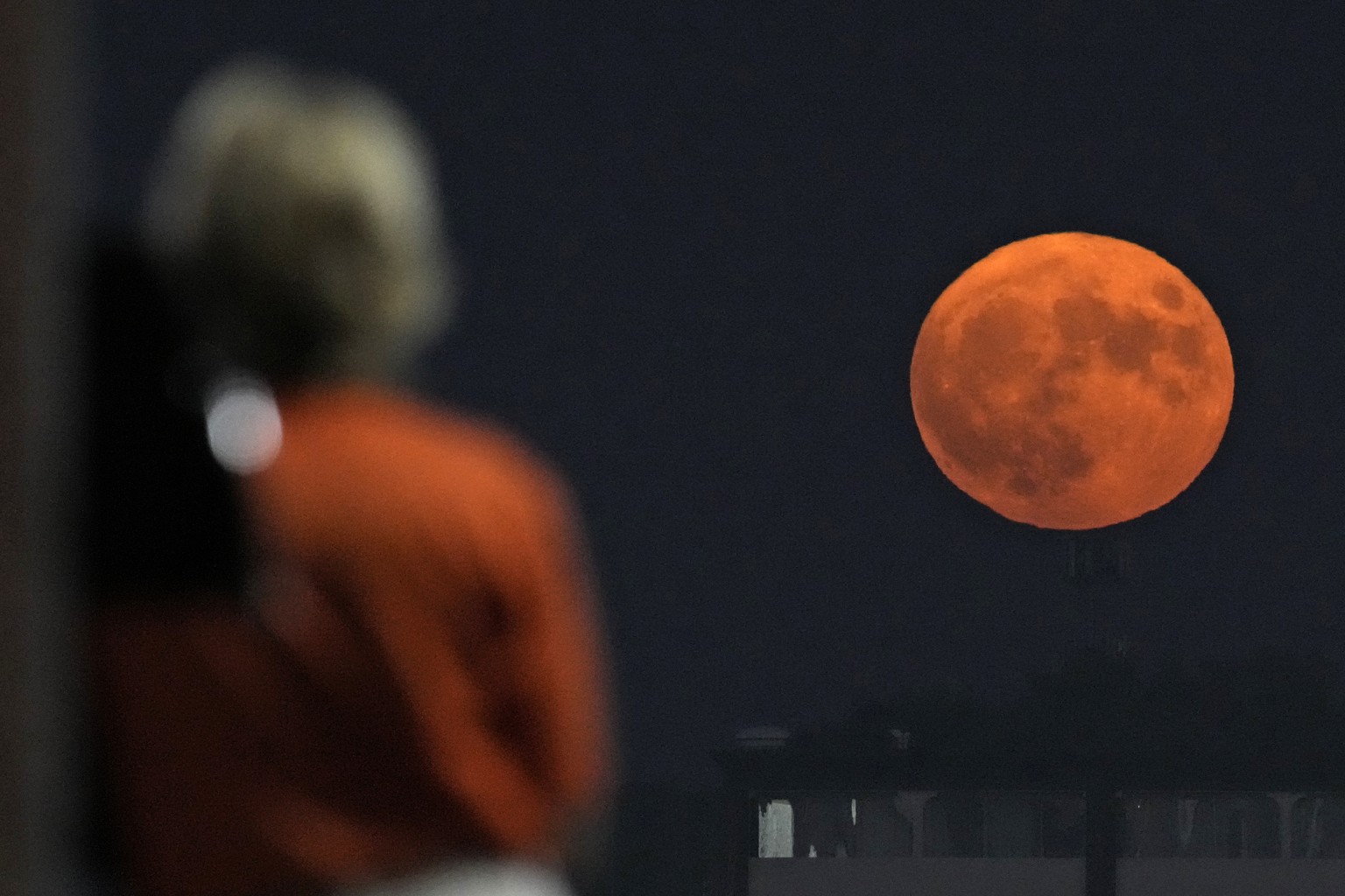 A woman watches from the upper deck of a baseball game between the Kansas City Royals and the Pittsburgh Pirates as the moon rises in the distance Wednesday, Aug. 30, 2023, in Kansas City, Mo. The moo ...