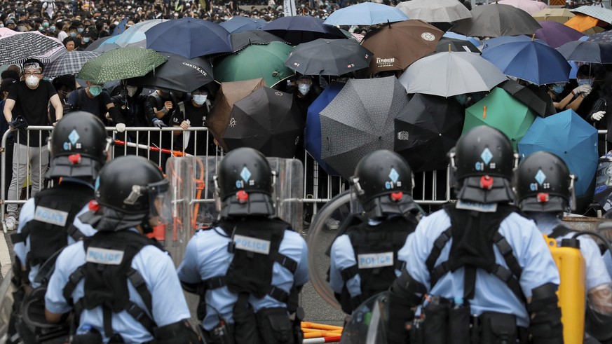 FILE - In this file photo taken Wednesday, June 12, 2019, policemen in riot gear stand watch as protesters use umbrellas to shield themselves near the Legislative Council in Hong Kong. Hong Kong&#039; ...