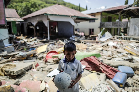 epa07065868 A seven-year-old boy, Taufikurahman, holds a plastic soccer ball on the rubble of a collapsed house at a tsunami devastated area in Donggala, Central Sulawesi, Indonesia, 03 October 2018.  ...