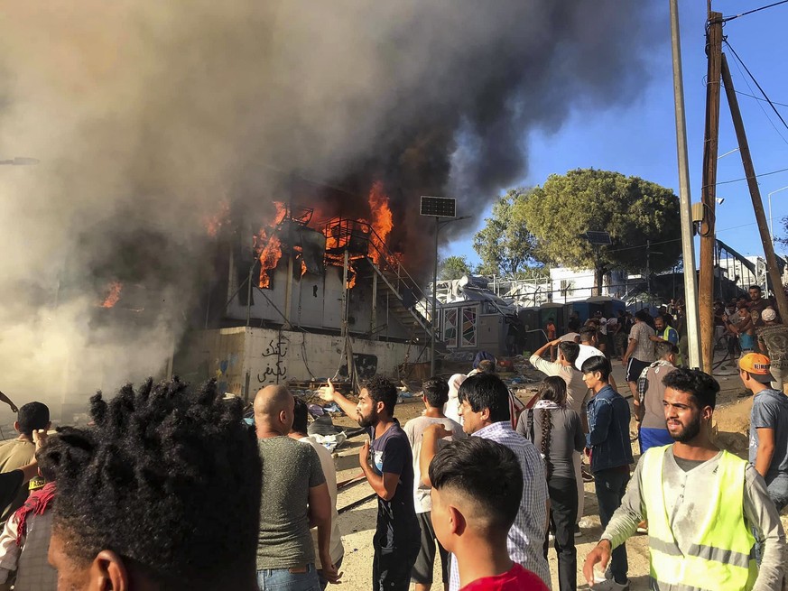 Migrants and refugees stand next to burning house containers at the Moria refugee camp, on the northeastern Aegean island of Lesbos, Greece, Sunday, Sept. 29, 2019. Migrants protesting at an overcrowd ...