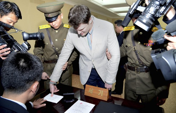 epa05214148 A photo provided by the official Korean Central News Agency (KCNA) on 16 March 2016 shows US student (C) placing fingerprints on documents in relation to his trial held by The Supreme Cour ...