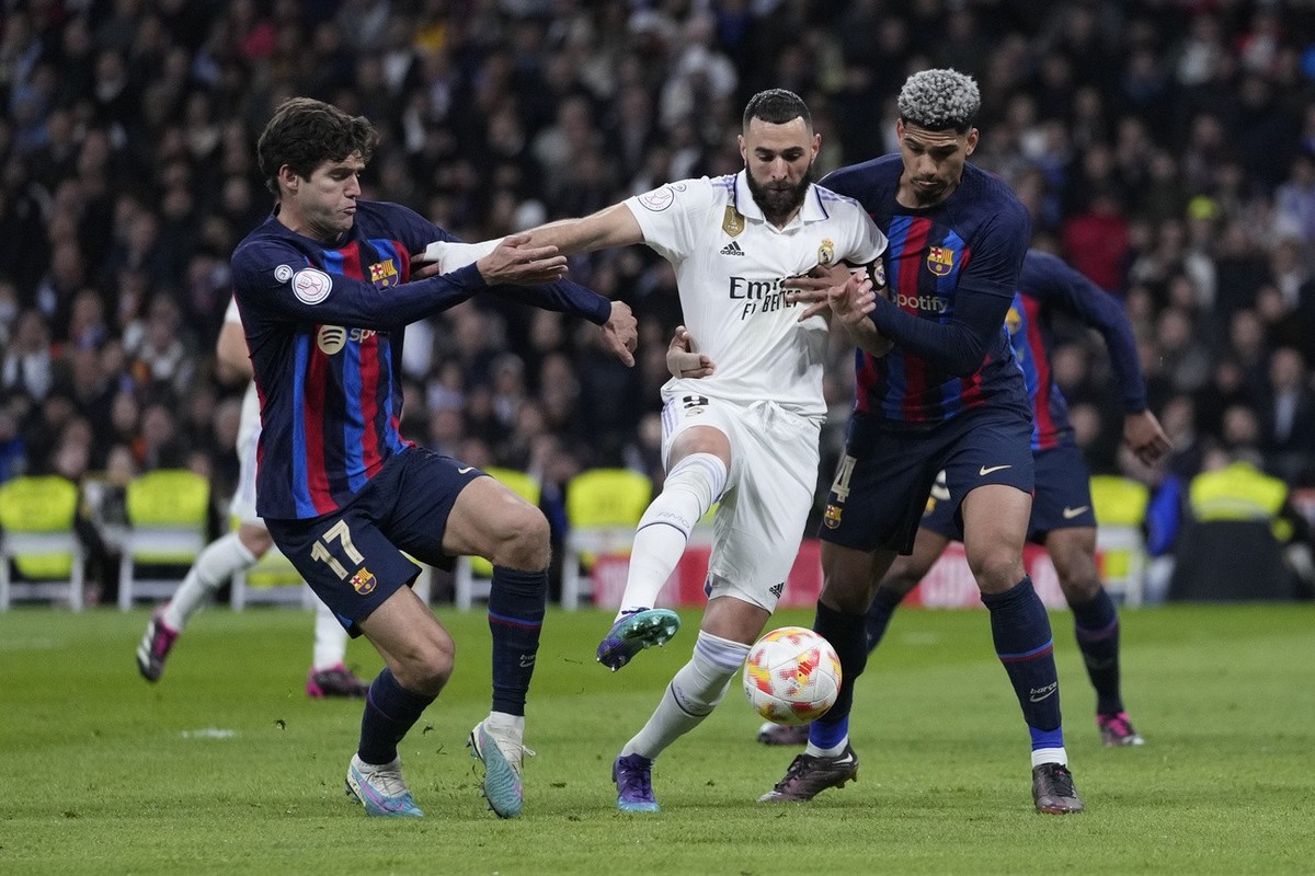 Real Madrid's Karim Benzema, centre, fights for the ball with Barcelona's Ronald Araujo, right, and Barcelona's Marcos Alonso during the Spanish Copa del Rey semi final, first leg socce ...