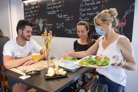 epa09238643 A waitress wearing a face protection mask serves lunch inside the restaurant &#039;Le 23.6&#039; during the re-opening day of restaurants, in Porrentruy, Switzerland, 31 May 2021. A number ...